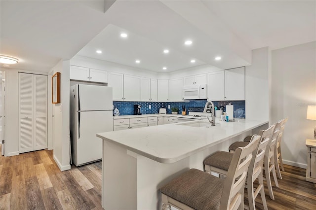 kitchen featuring backsplash, white cabinets, white appliances, a peninsula, and a kitchen breakfast bar