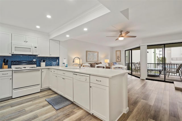 kitchen featuring light countertops, white cabinets, a sink, white appliances, and a peninsula