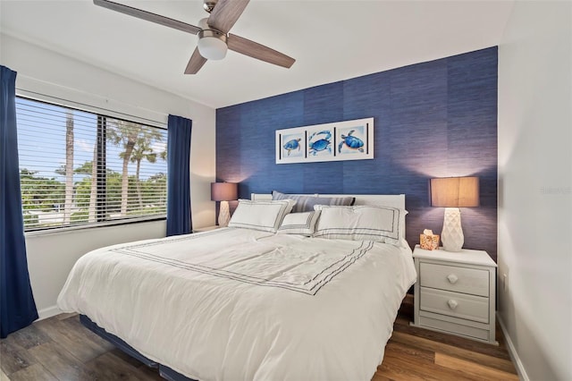 bedroom with an accent wall, dark wood-style flooring, a ceiling fan, and baseboards