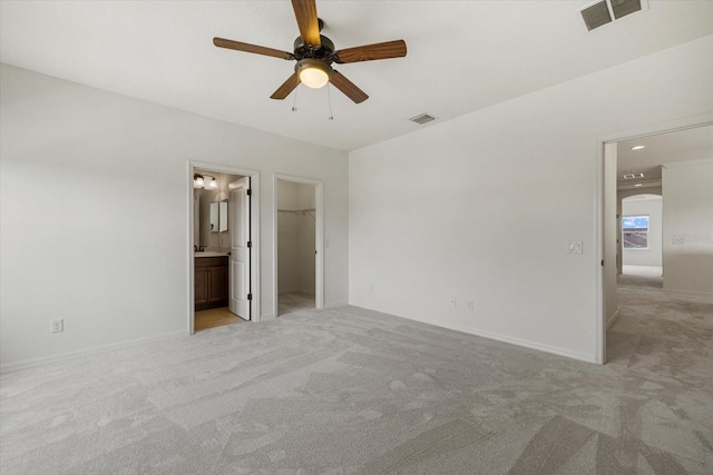 unfurnished bedroom with light carpet, ceiling fan, a walk in closet, connected bathroom, and a closet