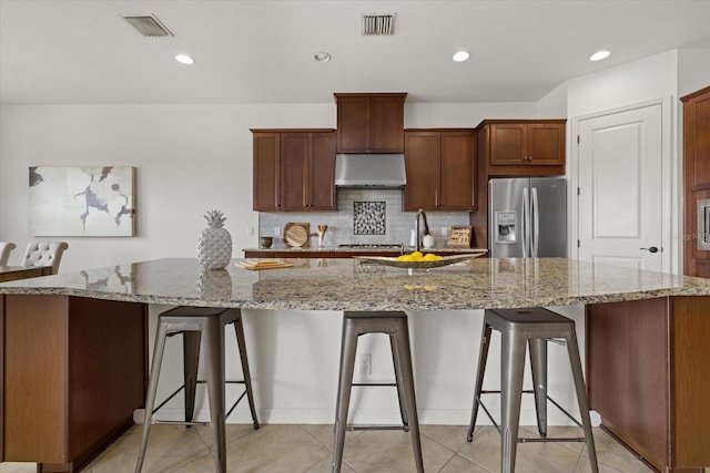 kitchen featuring stainless steel refrigerator with ice dispenser, sink, a spacious island, and light stone counters