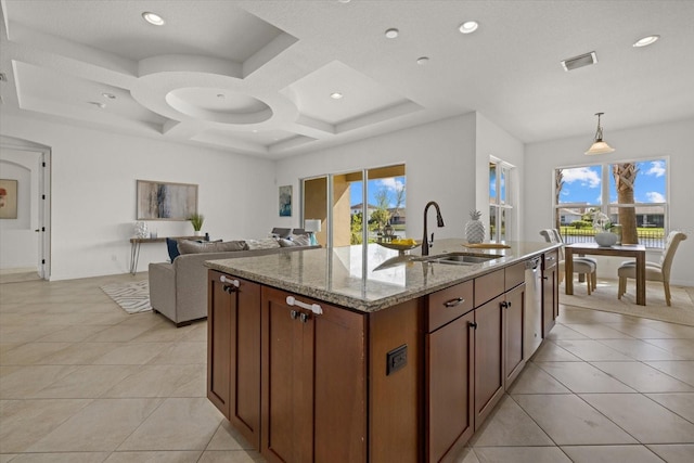 kitchen with light stone counters, pendant lighting, coffered ceiling, sink, and an island with sink