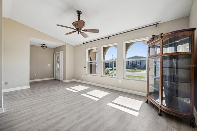 empty room with ceiling fan, vaulted ceiling, and light hardwood / wood-style flooring