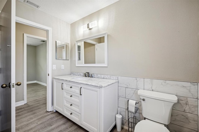 bathroom featuring toilet, vanity, hardwood / wood-style floors, tile walls, and a textured ceiling