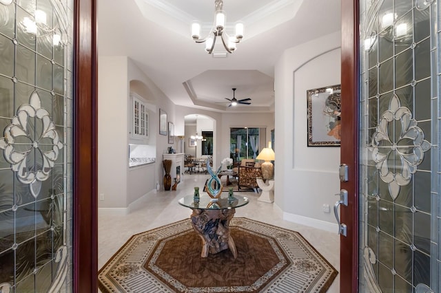 foyer entrance featuring ceiling fan with notable chandelier, a raised ceiling, and crown molding