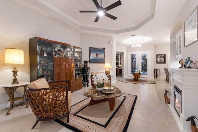 tiled living room with french doors, ornamental molding, ceiling fan with notable chandelier, and a raised ceiling