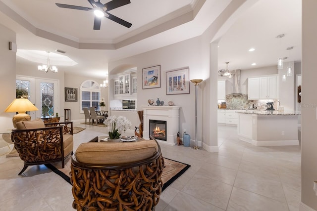 living room with ceiling fan with notable chandelier, a tray ceiling, light tile patterned floors, and ornamental molding