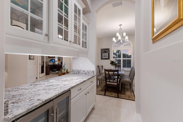 bar featuring light stone counters, decorative light fixtures, a chandelier, and white cabinetry