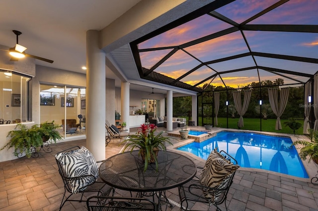 pool at dusk with ceiling fan, glass enclosure, and a patio area