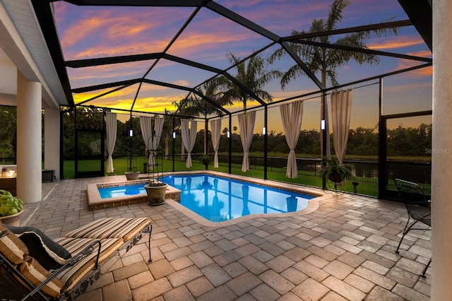 pool at dusk with a patio, an in ground hot tub, and glass enclosure