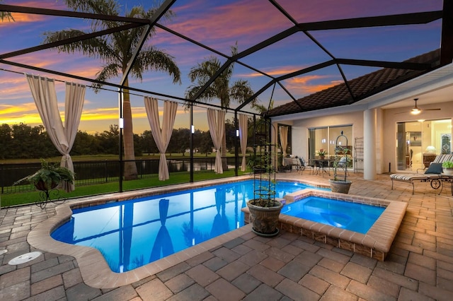 pool at dusk with a patio, glass enclosure, and ceiling fan