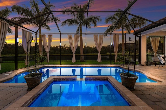 pool at dusk featuring glass enclosure, an in ground hot tub, and a patio area