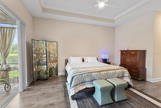 bedroom with ceiling fan, ornamental molding, hardwood / wood-style floors, a tray ceiling, and access to exterior