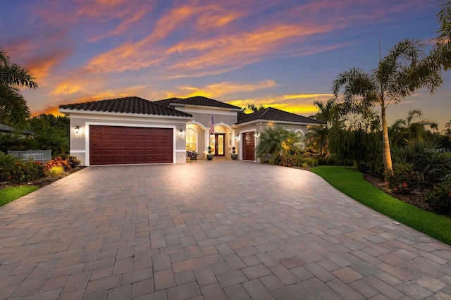 mediterranean / spanish-style home with a garage, a tiled roof, decorative driveway, and stucco siding