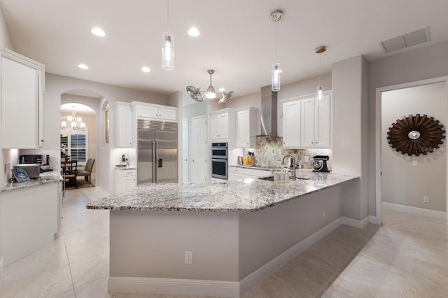 kitchen featuring stainless steel appliances, white cabinetry, wall chimney range hood, and decorative light fixtures