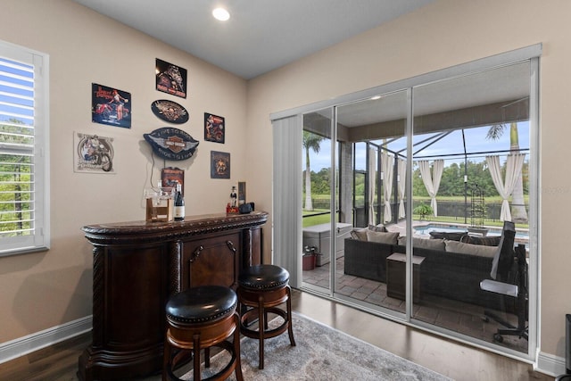 bar with baseboards, a sunroom, wood finished floors, a bar, and recessed lighting