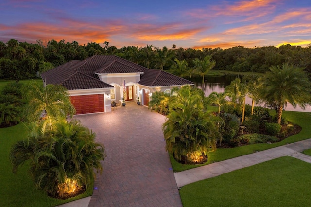 mediterranean / spanish house featuring an attached garage, a water view, a tile roof, decorative driveway, and a front yard