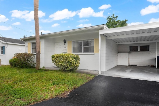 exterior space featuring a carport, a front lawn, concrete block siding, and aphalt driveway