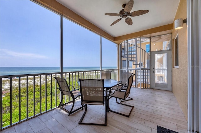 sunroom / solarium featuring a water view, a healthy amount of sunlight, ceiling fan, and a view of the beach