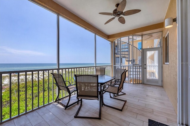 sunroom / solarium featuring ceiling fan, a beach view, and a water view