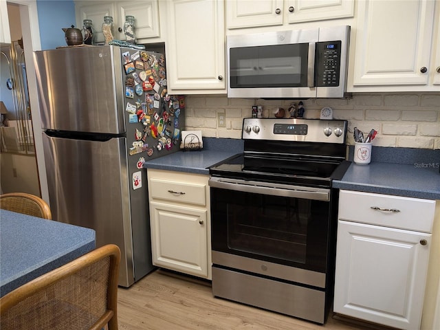 kitchen featuring dark countertops, light wood-style flooring, appliances with stainless steel finishes, white cabinetry, and backsplash