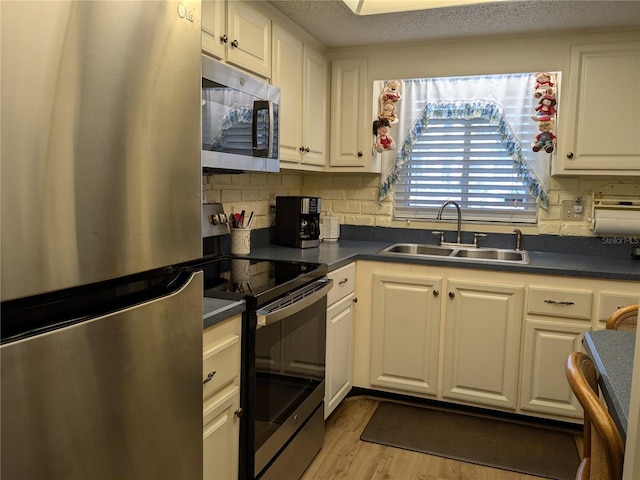 kitchen with appliances with stainless steel finishes, dark countertops, white cabinets, and a sink