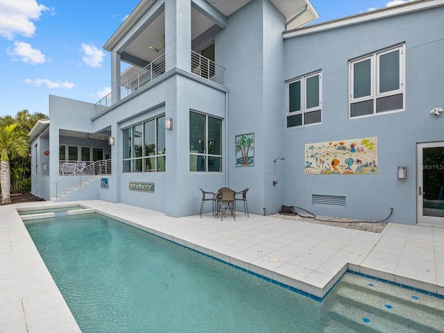 back of property featuring a balcony, visible vents, stucco siding, an outdoor pool, and a patio area