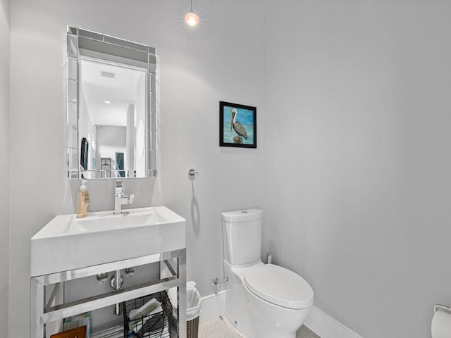 half bathroom with baseboards, visible vents, a sink, and toilet