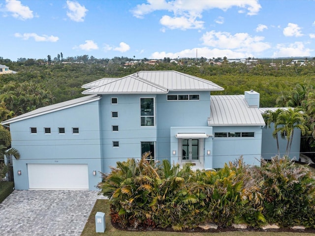 view of front facade featuring decorative driveway, stucco siding, a standing seam roof, metal roof, and a garage