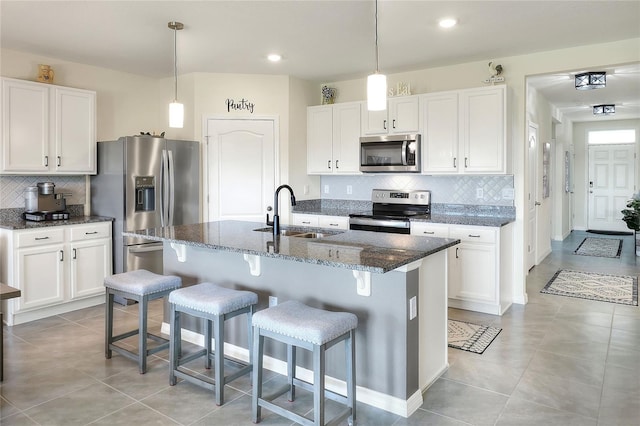 kitchen featuring dark stone countertops, sink, appliances with stainless steel finishes, a center island with sink, and white cabinets