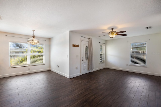 empty room with dark hardwood / wood-style floors, a textured ceiling, ceiling fan with notable chandelier, and a wealth of natural light