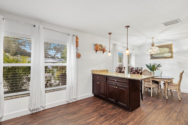 kitchen with a wealth of natural light, dark wood-type flooring, light stone countertops, and pendant lighting