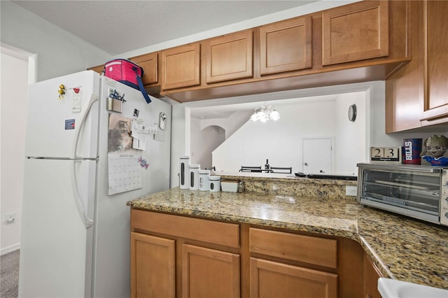 10959 Keys Gate Dr, Riverview, FL 33579 - kitchen with a notable chandelier, brown cabinetry, light stone counters, a toaster, and freestanding refrigerator