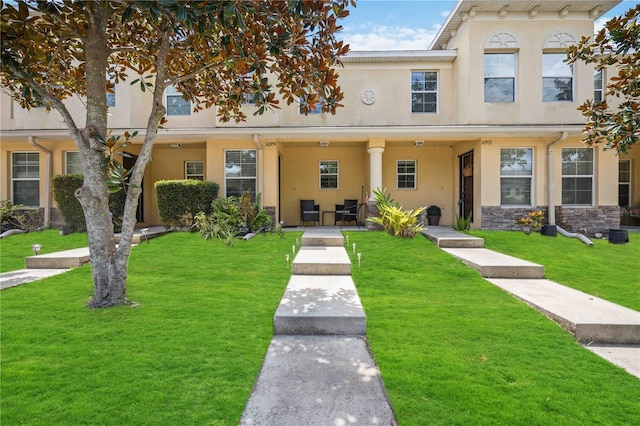 townhome / multi-family property with a front yard, stone siding, and stucco siding