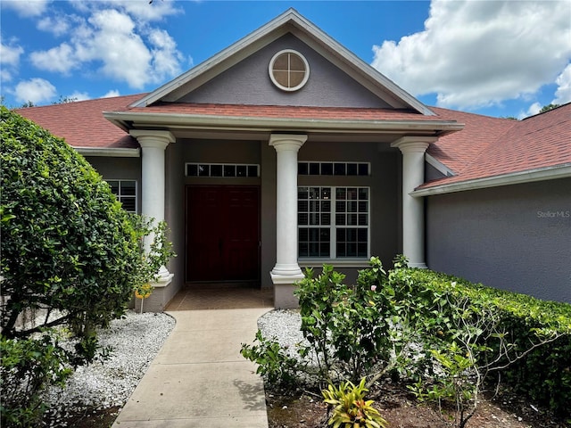 view of exterior entry featuring roof with shingles and stucco siding