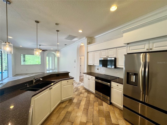 kitchen featuring arched walkways, dark countertops, appliances with stainless steel finishes, pendant lighting, and a sink