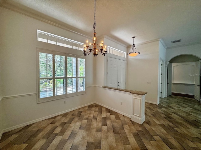 unfurnished dining area with a textured ceiling, a notable chandelier, ornamental molding, and dark hardwood / wood-style floors