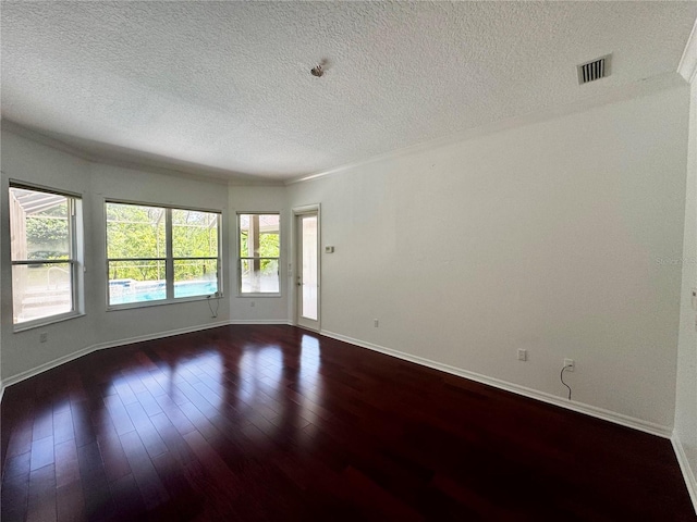 spare room with a textured ceiling, dark wood-type flooring, visible vents, and baseboards