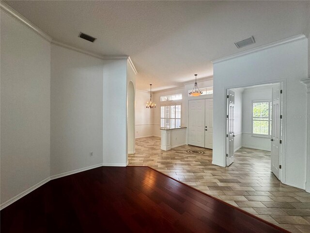 unfurnished living room featuring light wood-type flooring, crown molding, a textured ceiling, and an inviting chandelier