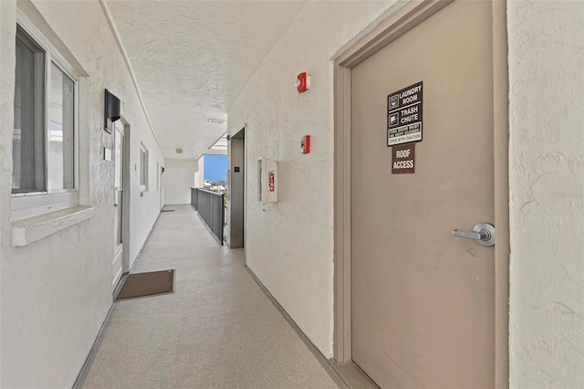 hallway with elevator, a textured wall, and a textured ceiling