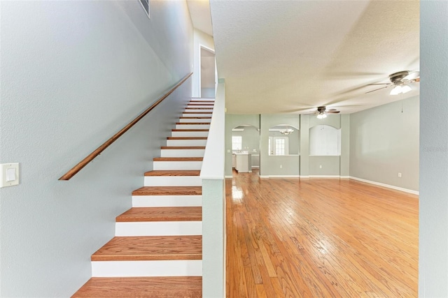 staircase with ceiling fan, hardwood / wood-style flooring, and a textured ceiling