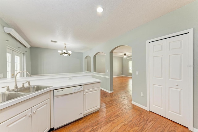 kitchen featuring light wood-type flooring, white cabinetry, decorative light fixtures, white dishwasher, and sink