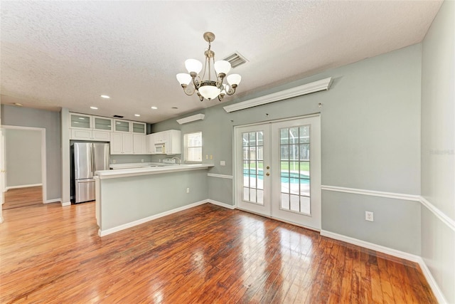 kitchen featuring decorative light fixtures, light hardwood / wood-style floors, kitchen peninsula, stainless steel refrigerator, and white cabinetry