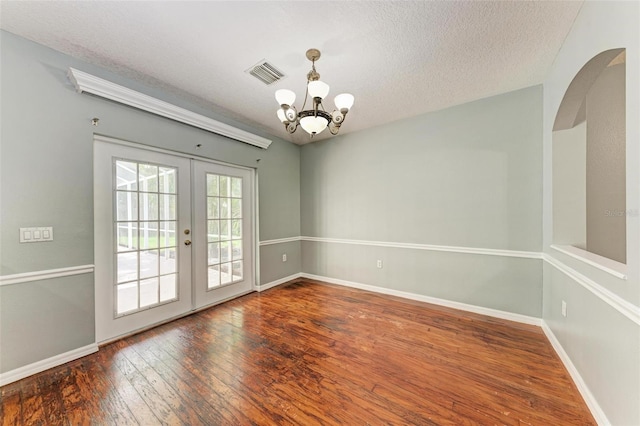 empty room with french doors, a textured ceiling, hardwood / wood-style floors, and an inviting chandelier