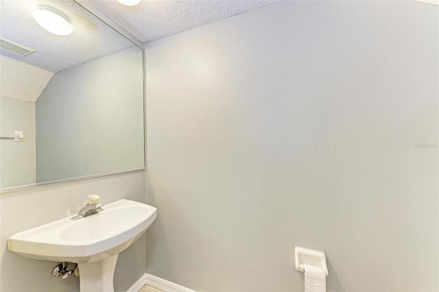 bathroom with lofted ceiling, sink, and a textured ceiling