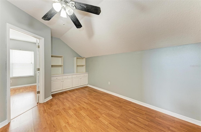 additional living space with ceiling fan, light hardwood / wood-style floors, a textured ceiling, and vaulted ceiling