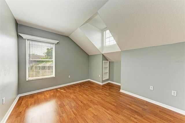 additional living space featuring vaulted ceiling, a textured ceiling, plenty of natural light, and light hardwood / wood-style floors