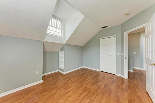 additional living space with a textured ceiling, light hardwood / wood-style flooring, and lofted ceiling