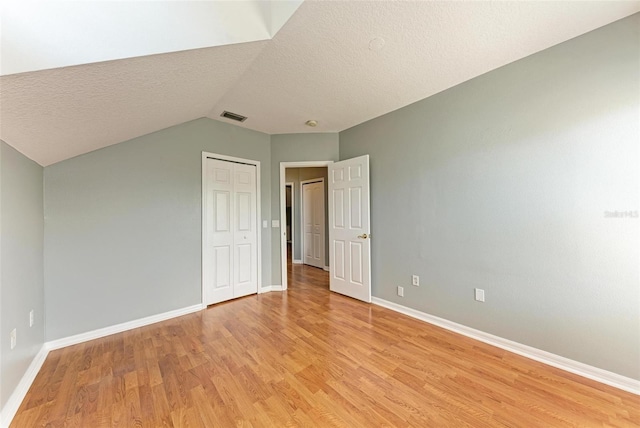 spare room with light wood-type flooring, a textured ceiling, and vaulted ceiling