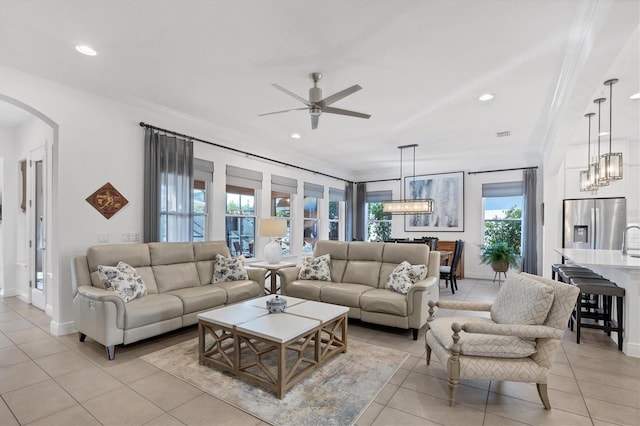 living room with ceiling fan with notable chandelier, light tile patterned floors, and crown molding